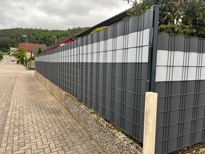 Doppelstabmattenzaun mit eingezogenen Sichtschutzstreifen über eine lange Flucht entlang einer Ortsstraße
