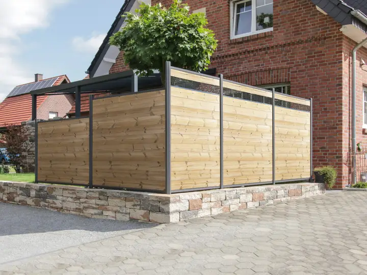 ThermoHolz-Sichtschutz mit dunklen Metallpfosten und schmalen Dekoreinsätzen um eine Terrasse auf einer Natursteinmauer